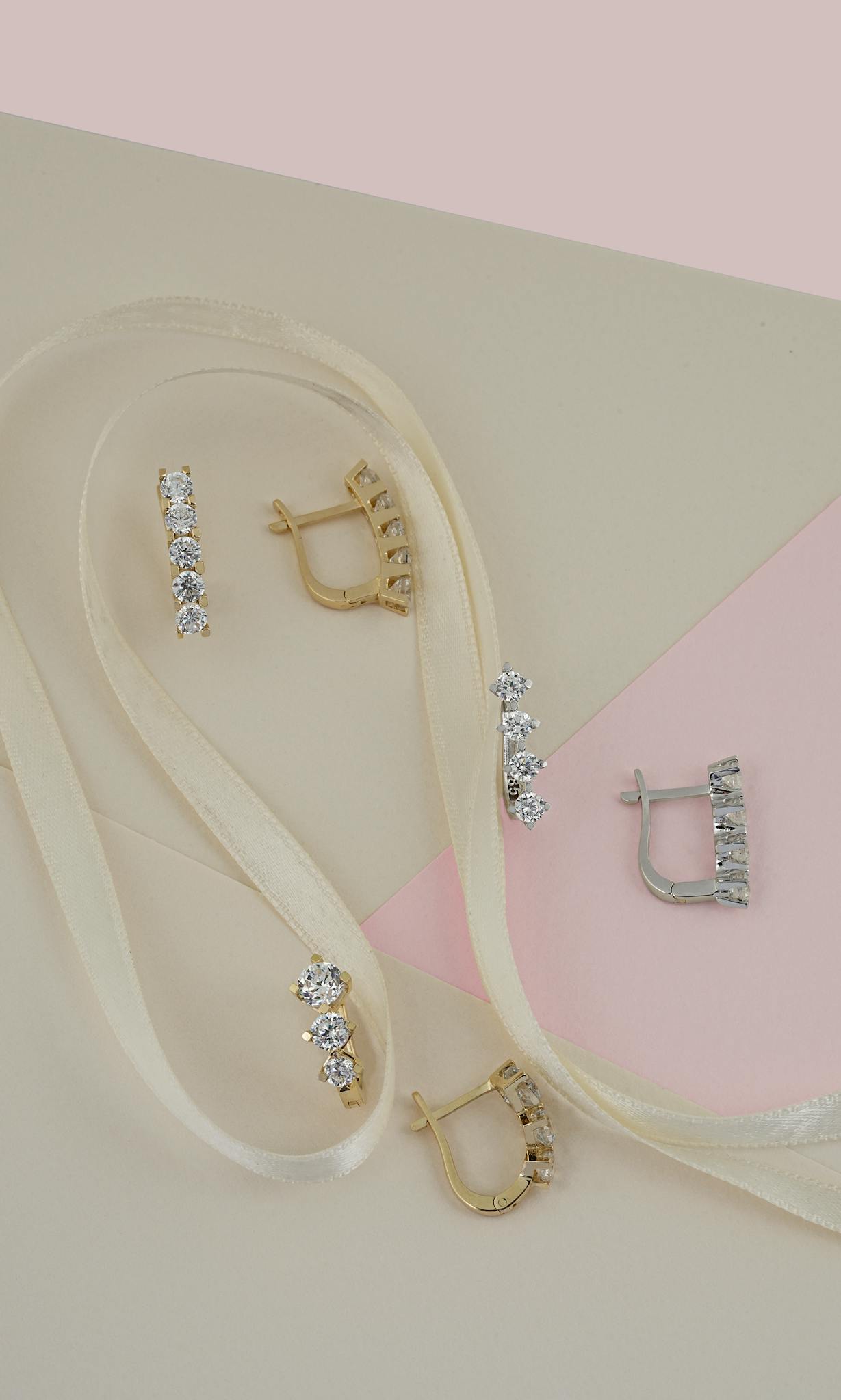 Elegant gold and silver earrings with diamonds on a pastel paper backdrop with ribbon.