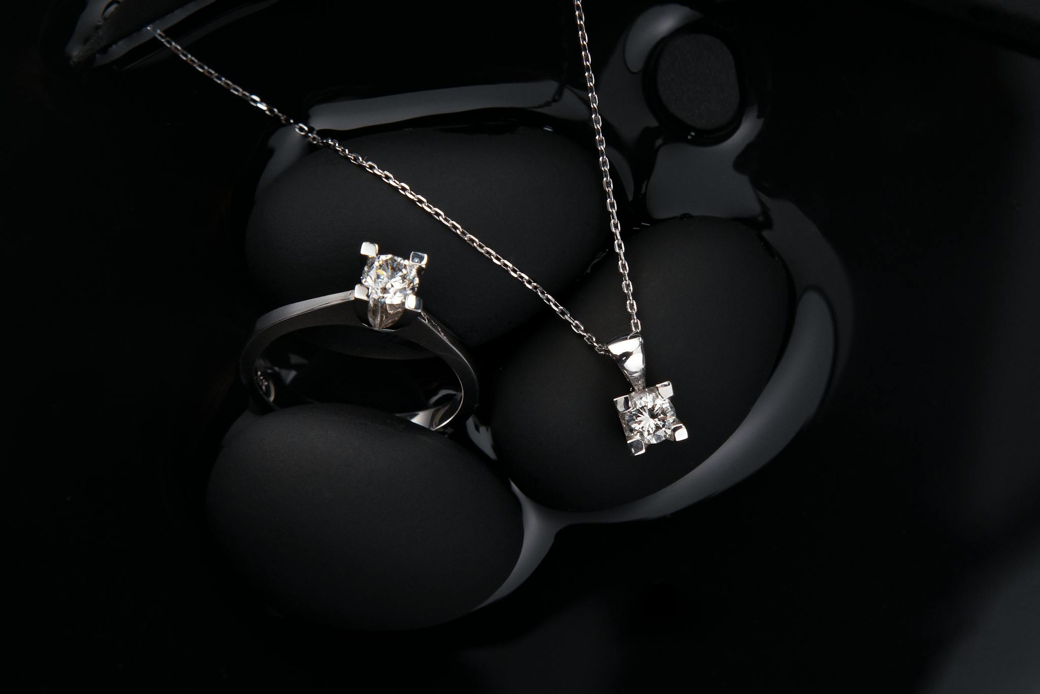 Luxurious silver diamond ring and pendant necklace on a black background, showcasing elegance and sophistication.